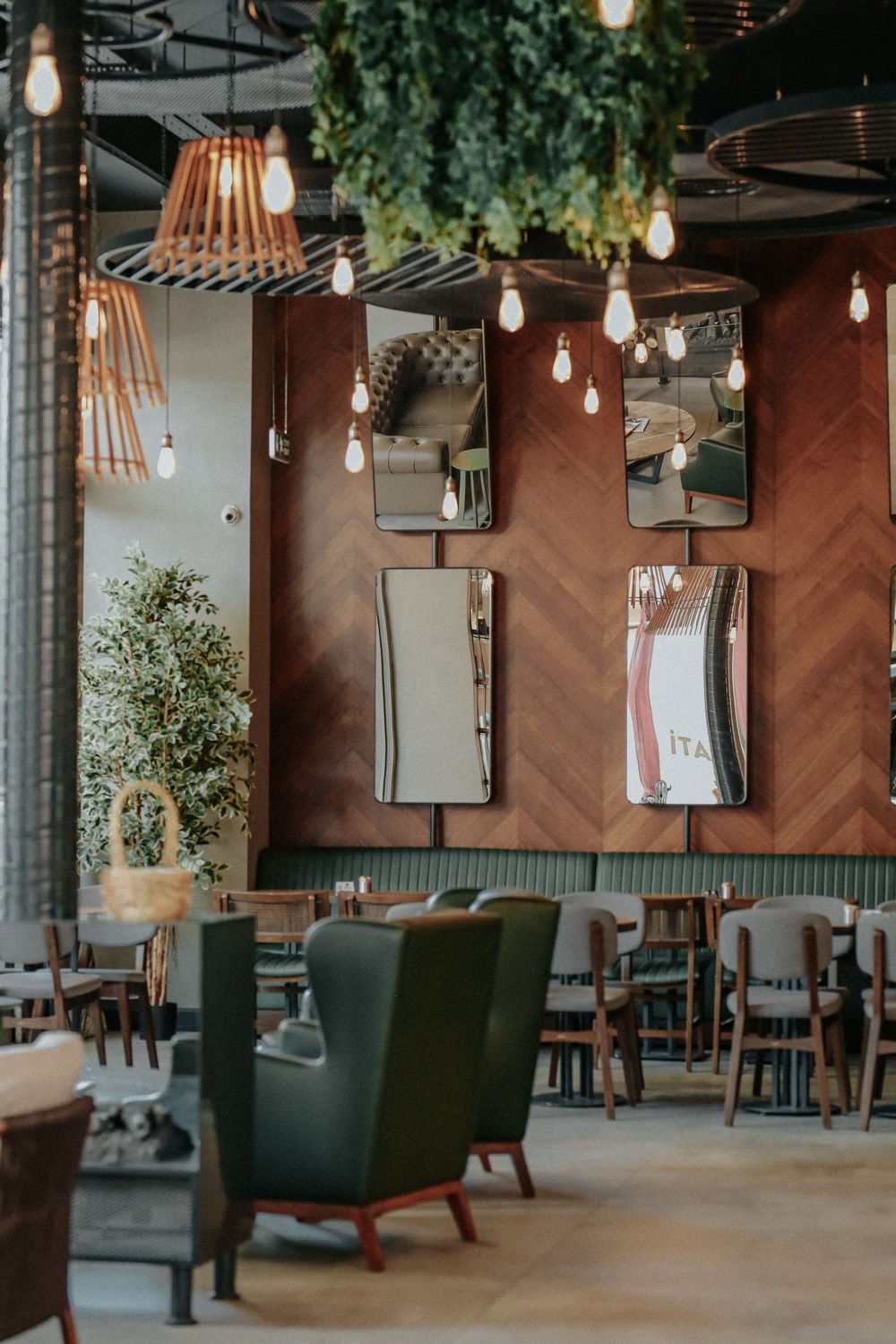 Restaurant dining room with green armchairs, wood-panelled walls and hanging lights