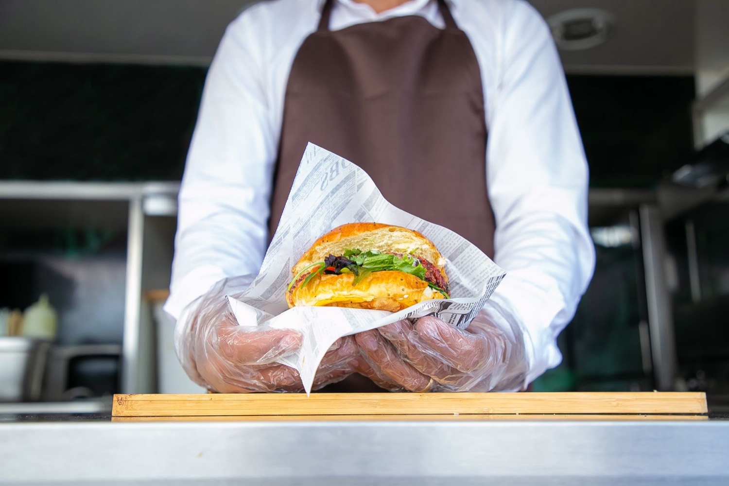 Cook in gloves holding a wrapped burger across a food truck counter