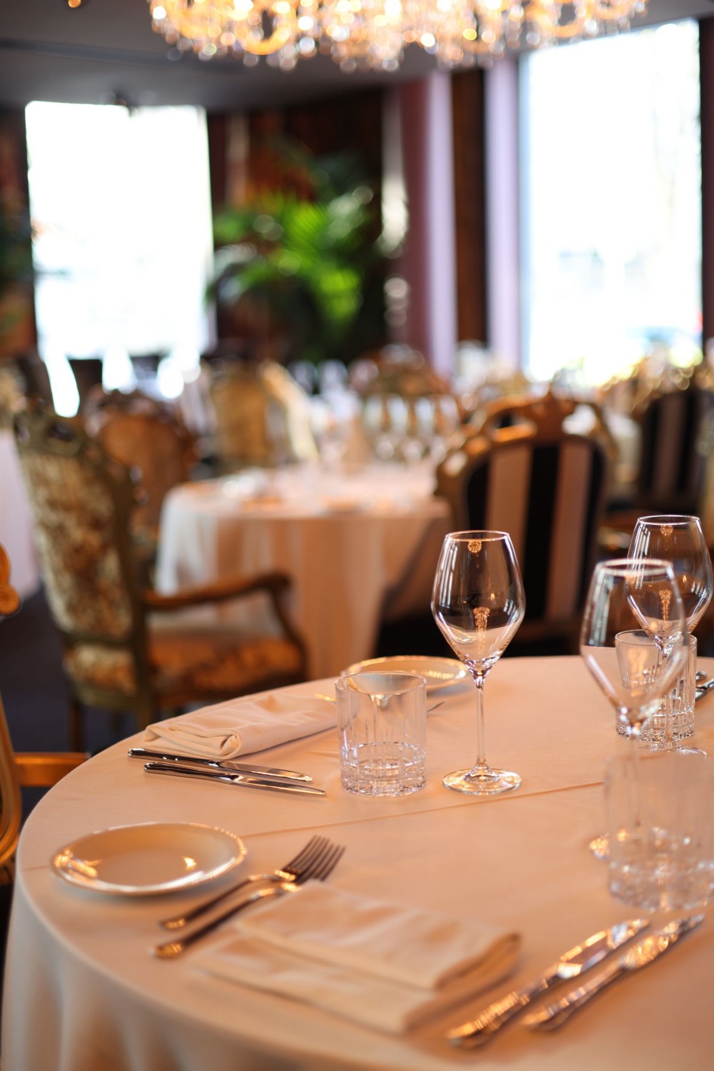 Fine dining tables set with white tablecloths and wine glasses under a chandelier
