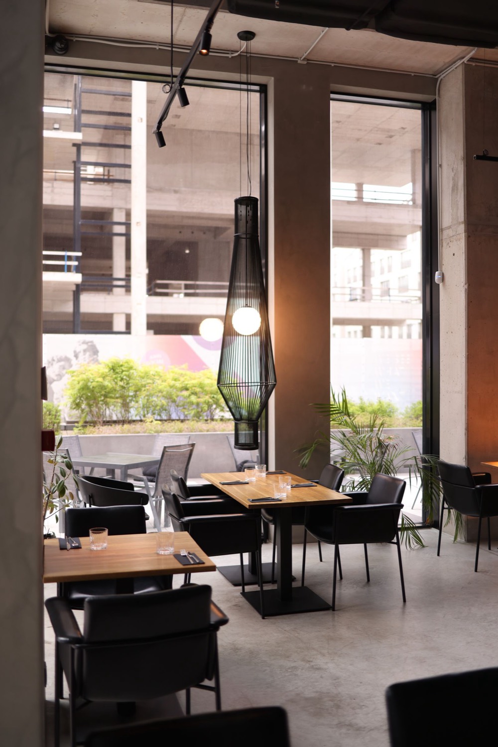 Modern restaurant with wooden tables, black chairs and tall windows